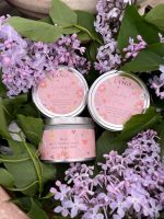 Three 'Wonderful Mum' soy candles in silver tins with pink floral labels, nestled in a bouquet of fresh purple lilacs.