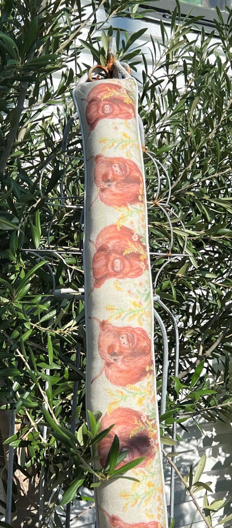 Dragstoppare med mönster av höglandsboskap och blommor, hängande i ett träd utomhus.