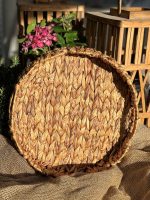 Stor rund flätad brödkorg i naturlig fiber på säckväv, med blommor och trälådor i bakgrunden.