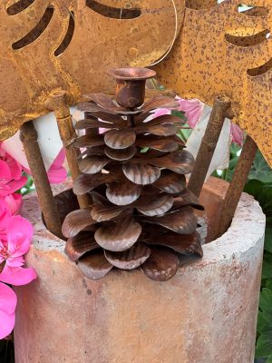 En rustik ljusstake i rostig plåt, formad som en grankotte, i en lerkruka med rosa blommor.